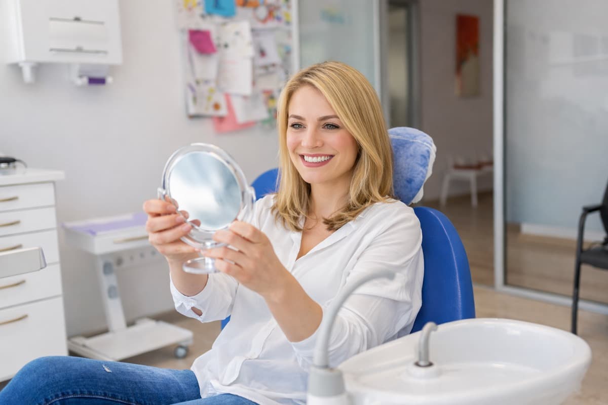 Implanturi în loc de proteză Bacău — pacientă fericită cu oglinda în cabinetul stomatologic, după consultația de implantologie pentru lucrare fixă pe implanturi la Chromatic Dental Clinic