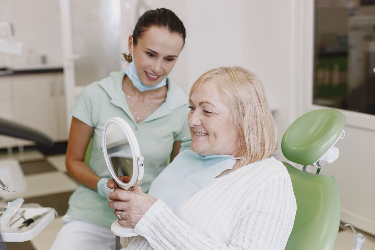 Pacientă care își verifică zâmbetul în oglindă la controlul după implant imediat, în Bacău