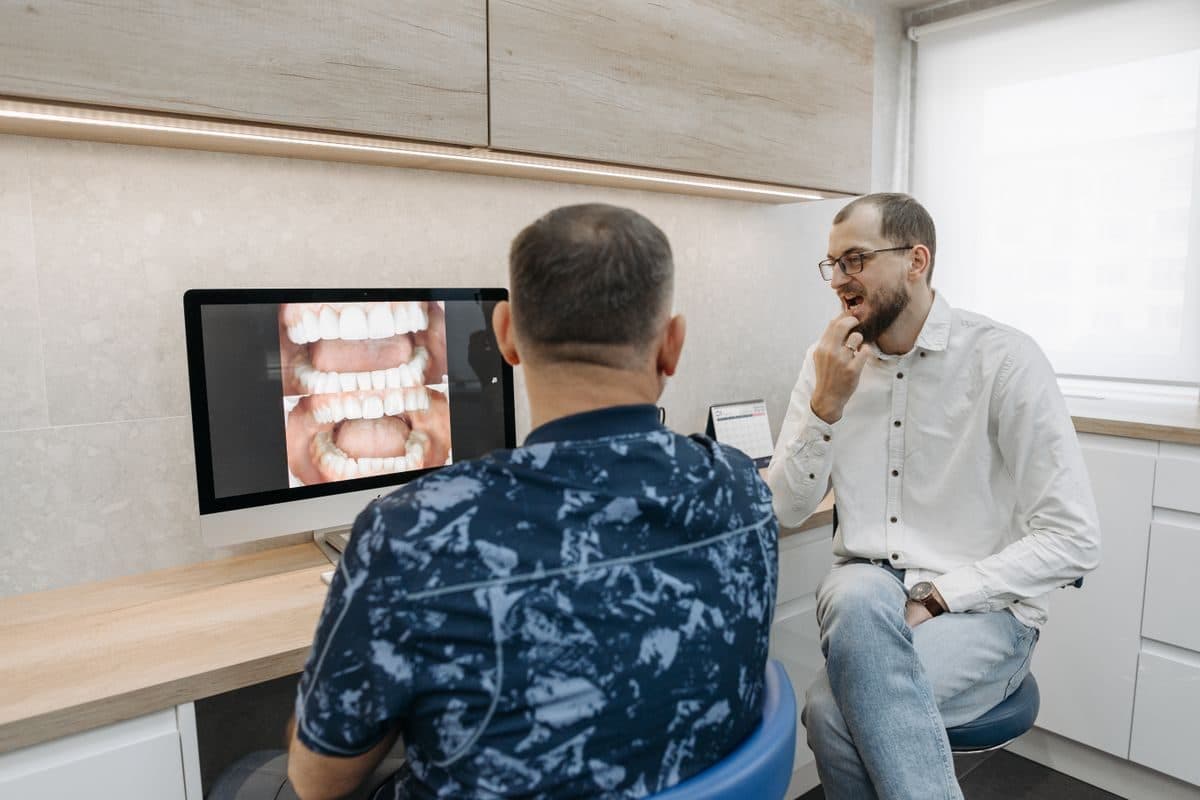 Medic stomatolog care discută cu pacientul imaginile de pe ecran la consultația pentru implant dentar în Bacău